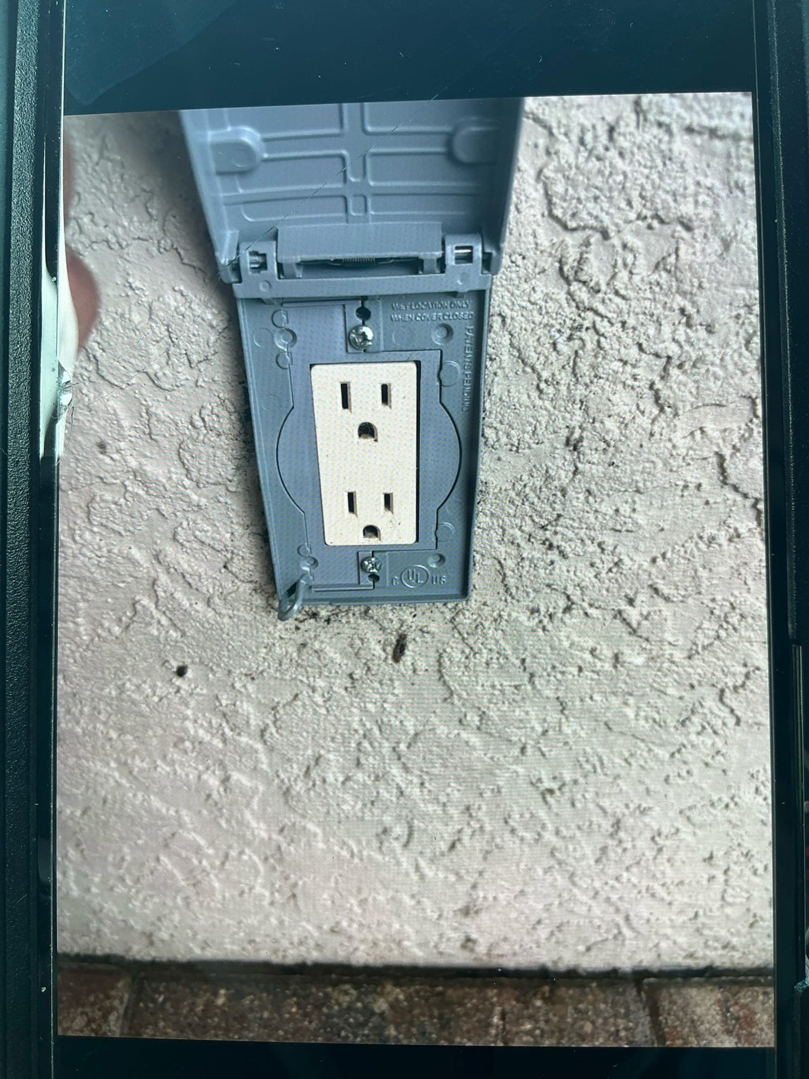 Standard 15-amp duplex outlet in gray weatherproof box with no GFCI protection visible.