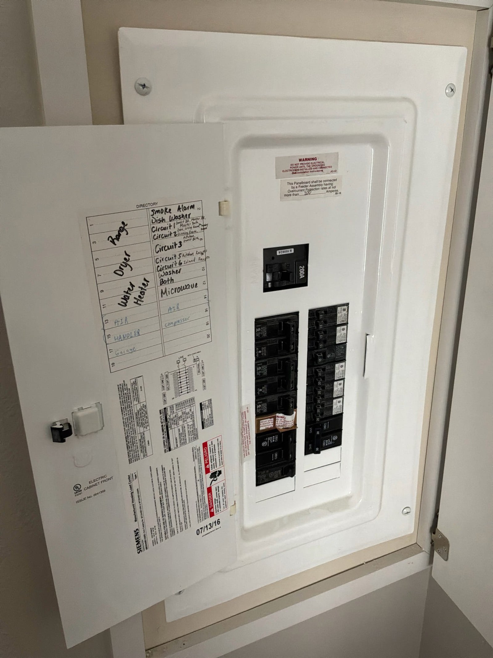 Electrical panel door open showing two-breaker configuration with handwritten directory label and multiple technical documents taped to interior door.