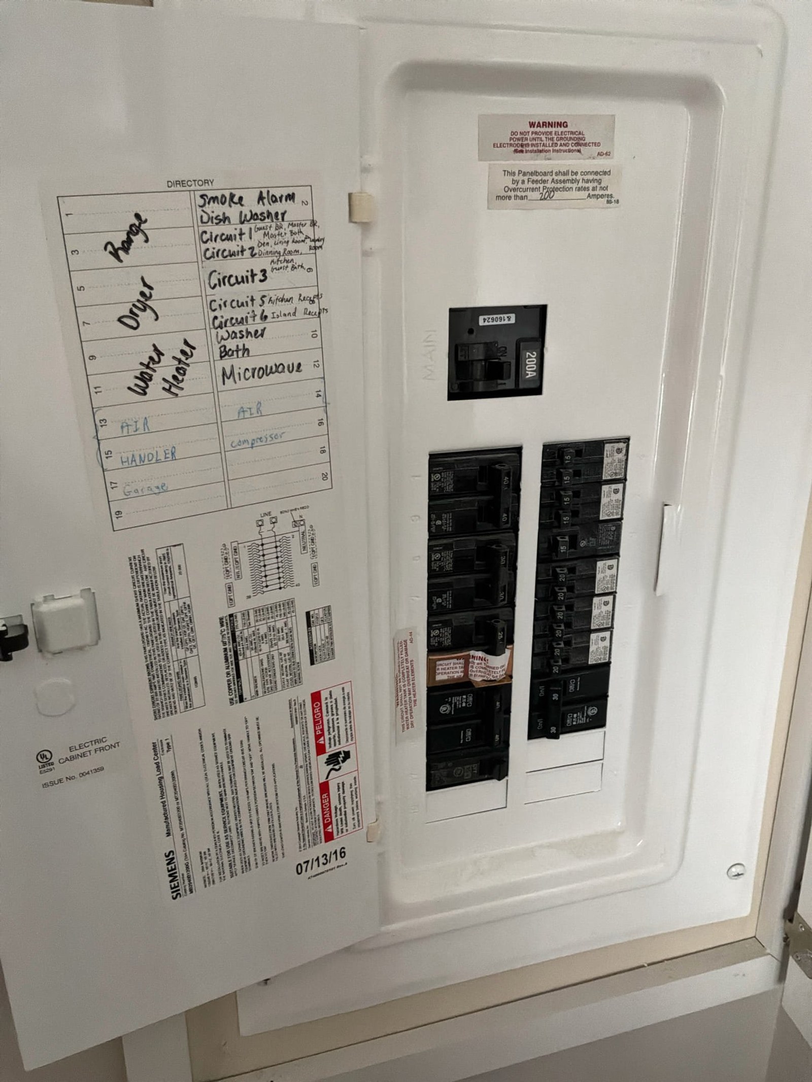 Electrical panel door open showing two-breaker configuration with handwritten directory label and multiple technical documents taped to interior door.