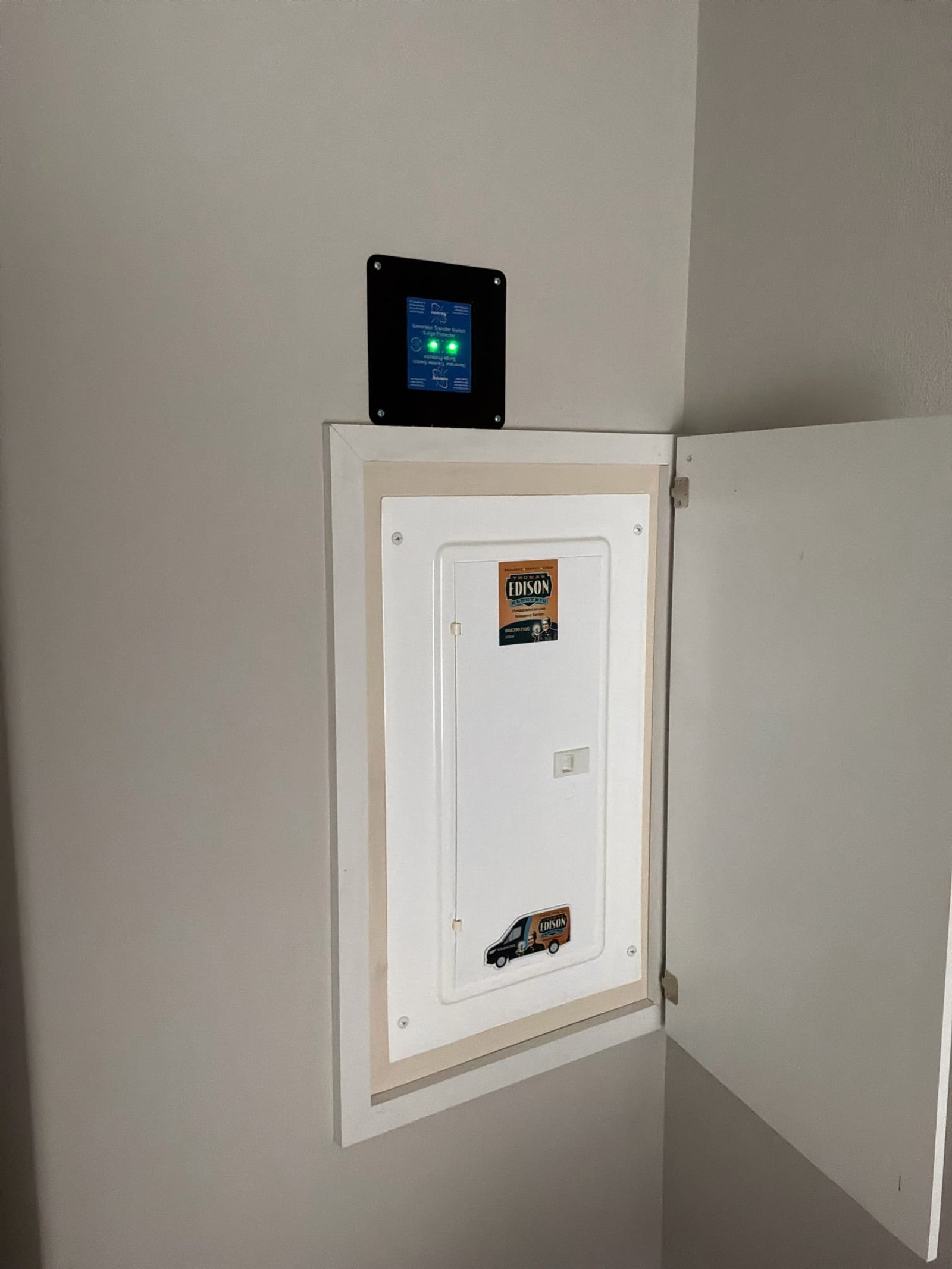 Newly installed surge protection device with digital monitoring display mounted above Edison brand electrical service entrance panel.